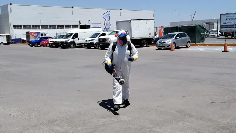 Toma panoramica de un estacionamiento con un fumigador caminando equipado con herramienta profesional para fumigar
