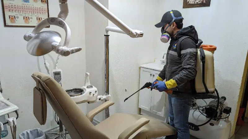 Fumigador profesional dentro de consultorio de dentista con herramienta para fumigar